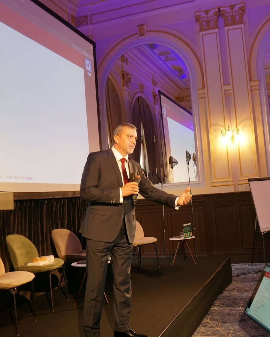 A speaker presenting on stage under the chandeliers at the 2026 edition of the Global Future of BPO, Shared Services & GBS Conference